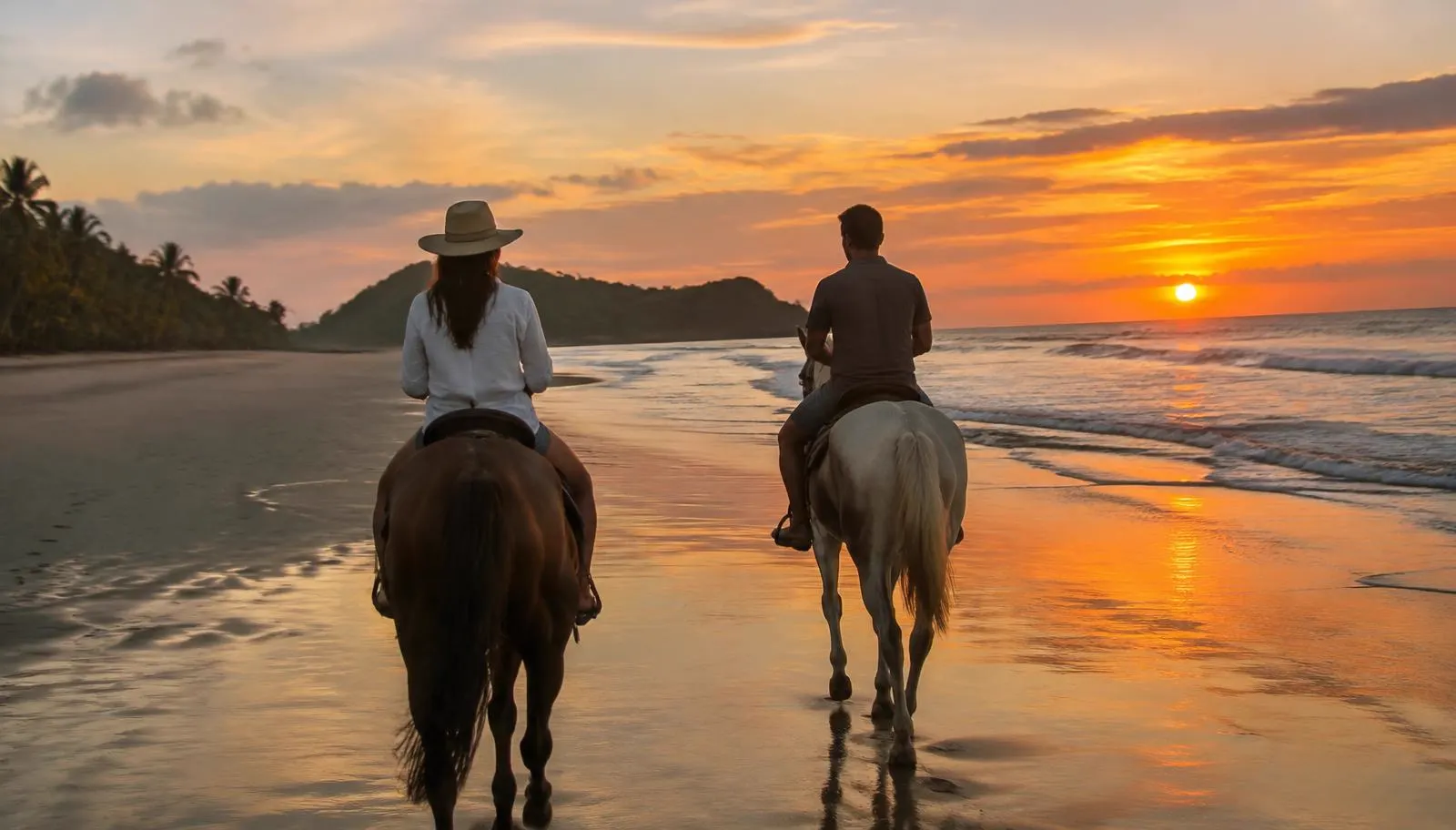Two riders on horseback along a Costa Rica beach at sunset